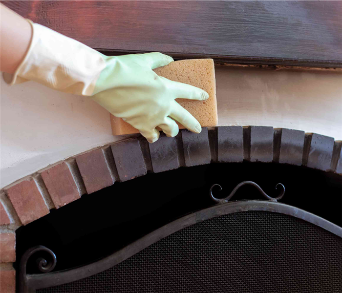 gloved hand using sponge to wipe soot above fireplace