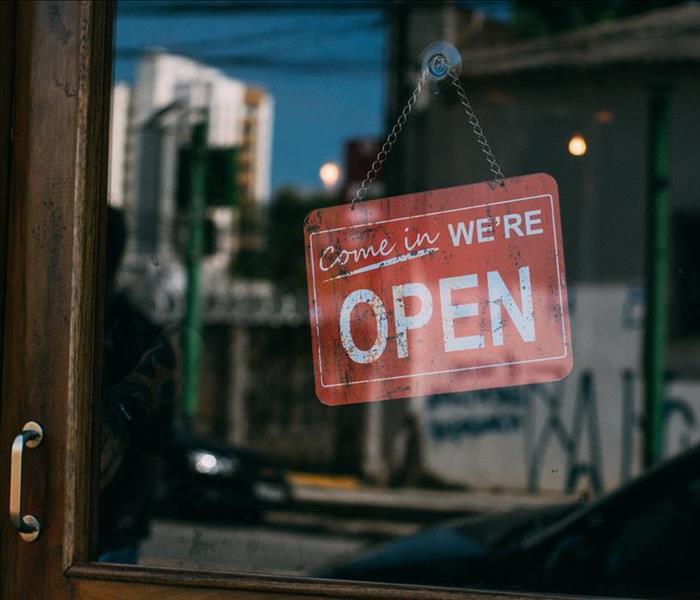 A red sign with white text reading “Come in We’re Open” hangs inside the window of a business.